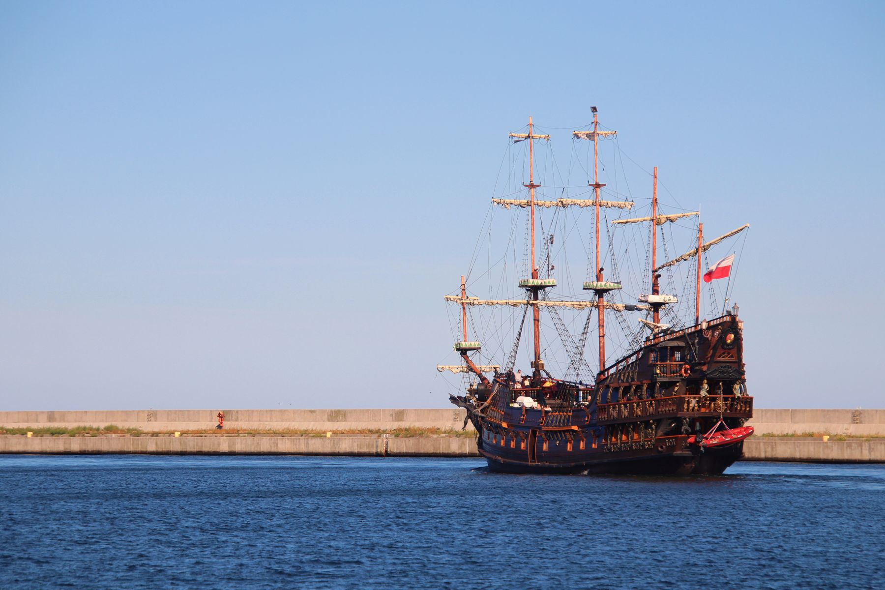 Galeón pirata de madera con los mástiles aparejados navegando bajo un cielo azul despejado