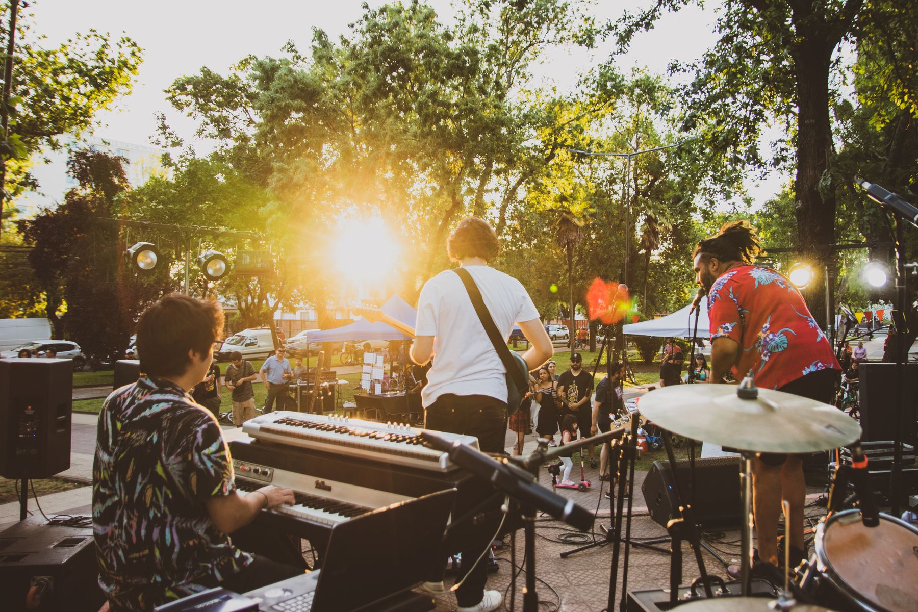Banda tocando en directo al aire libre en verano, con teclado, guitarra y batería entre los árboles